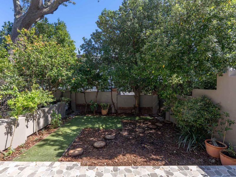 A private, low-maintenance garden featuring a combination of artificial turf, stone paving, and established trees enclosed by boundary walls.