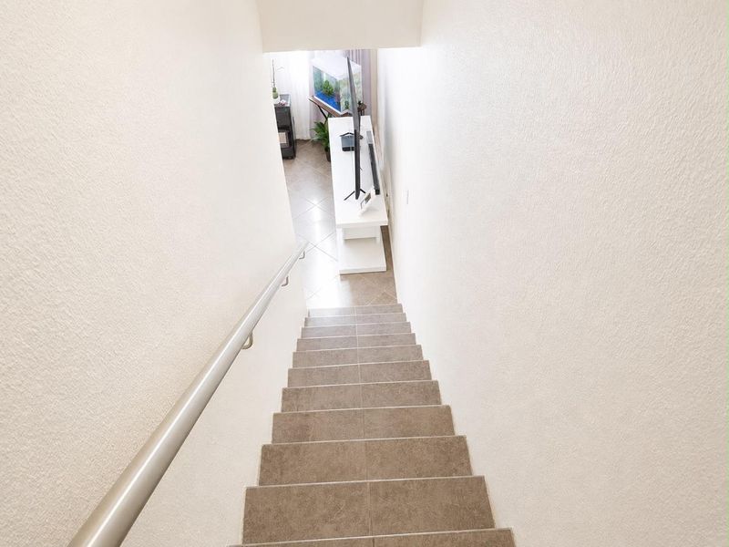 A view looking down a tiled staircase with a metal handrail, leading into a lower level living area.
