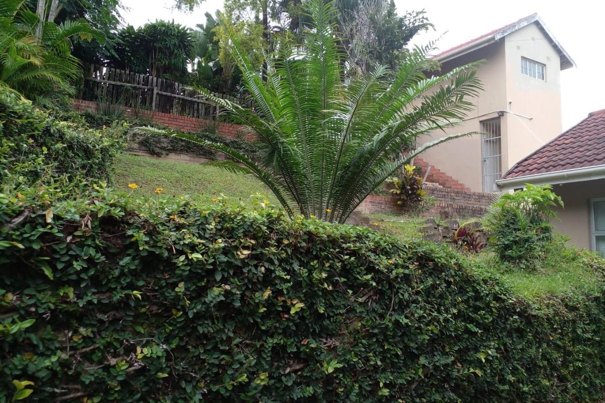 A view of the rear garden featuring terraced brick retaining walls, established landscaping, and a glimpse of the house exterior with tiled roofing.