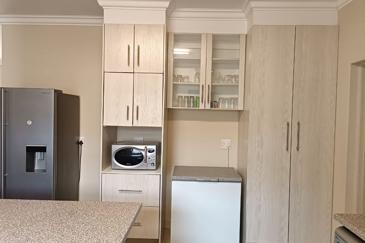 A well-maintained kitchen area featuring light wood-grain cabinetry, stone-look laminate countertops, and elegant crown molding, providing ample storage and a clean, functional workspace.
