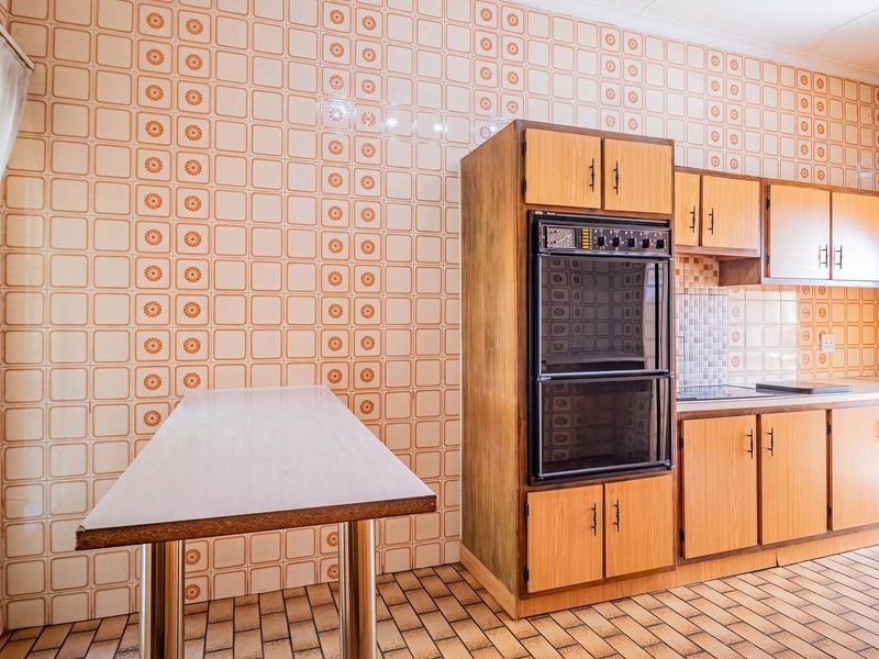 A dated kitchen featuring original patterned wall tiles, wood-look cabinetry, a built-in double oven, and tiled flooring.