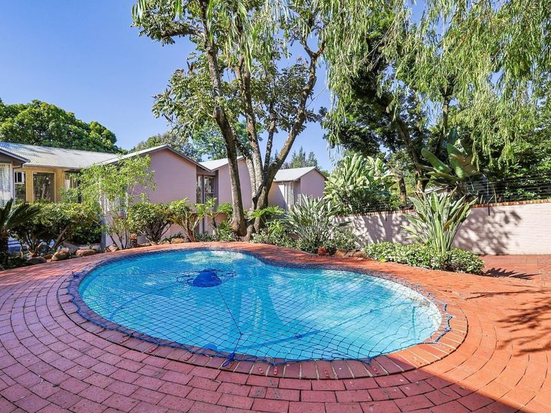 A private outdoor swimming pool area featuring brick paving, established garden landscaping, and a secure boundary wall in a townhouse setting.