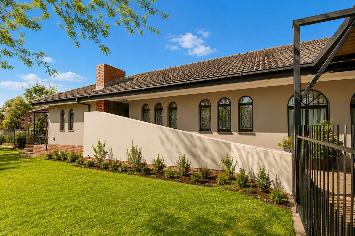A well-maintained rear exterior view of the house featuring a manicured lawn, arched windows, a brick chimney, and a modern ramp access.