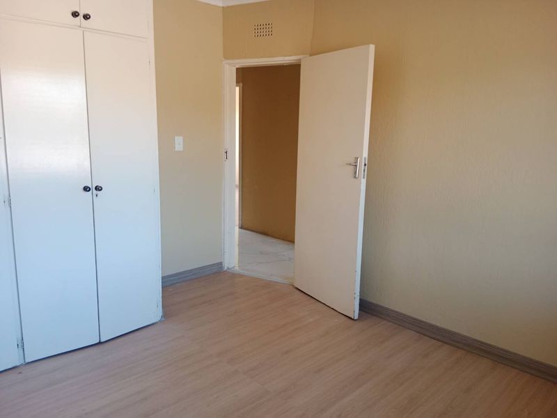 An empty bedroom featuring light-toned laminate flooring, built-in cupboards, and neutral wall finishes, offering a clean canvas for personalization.