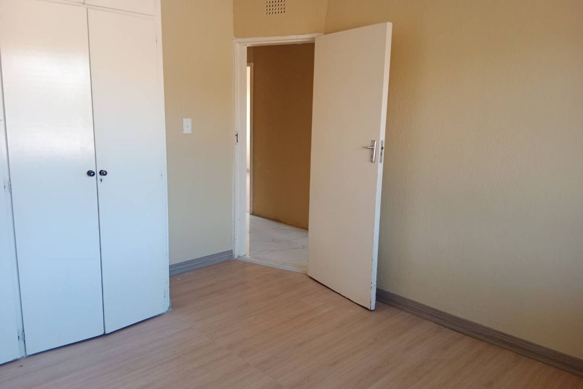 An empty bedroom featuring light-toned laminate flooring, built-in cupboards, and neutral wall finishes, offering a clean canvas for personalization.