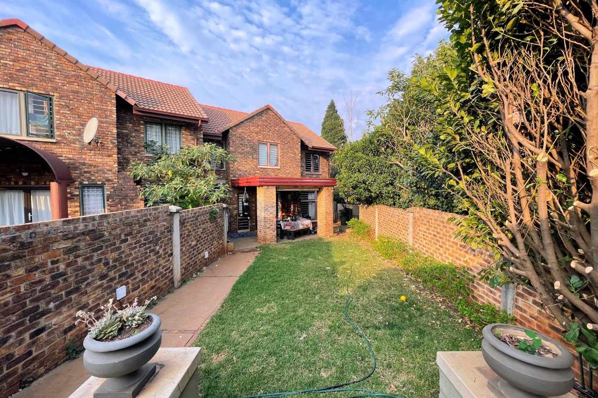 A rear view of a face brick townhouse featuring a private garden, lawn, paved walkway, and a covered patio area.