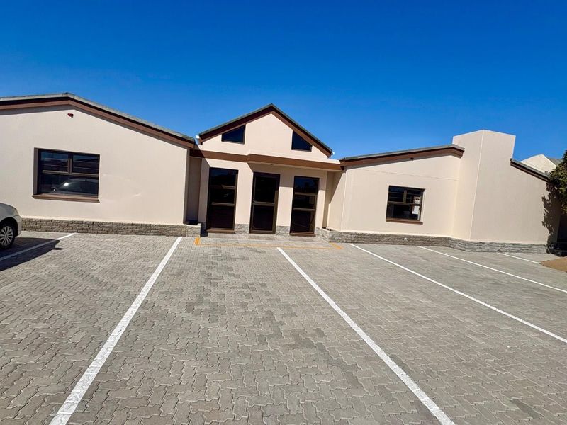 Front exterior view of a commercial office building featuring a paved parking area, stone cladding base, and multiple entrance points.