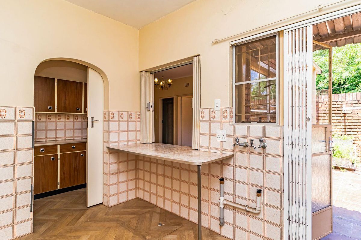 A dated kitchen area featuring a breakfast bar, tiled splashbacks, and direct access to an outdoor patio through a security gate.
