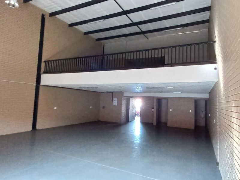 Spacious industrial warehouse unit featuring high ceilings, exposed brick walls, polished concrete flooring, and a mezzanine level with a safety railing.