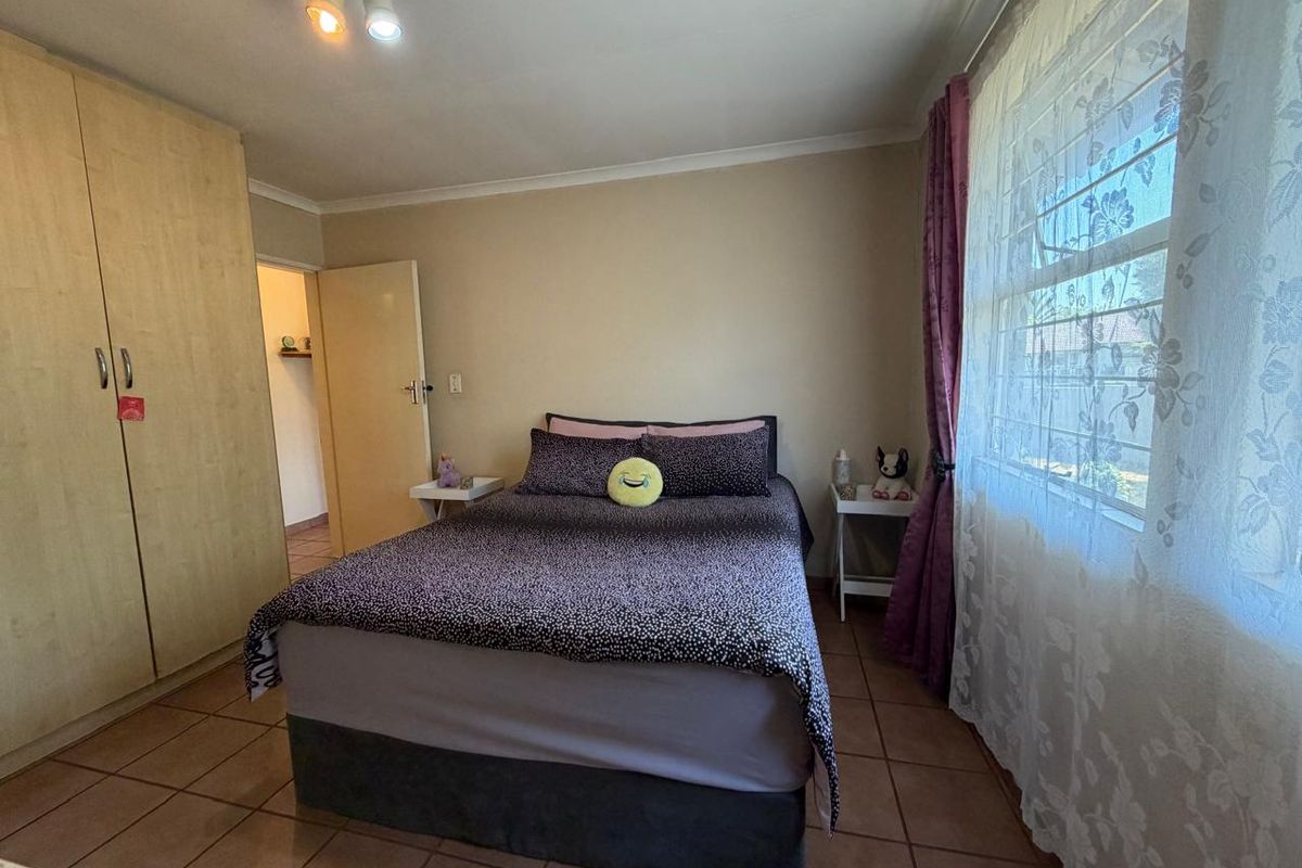 A functional bedroom featuring tiled flooring, a built-in wardrobe, and a window fitted with security bars, providing a practical living space.