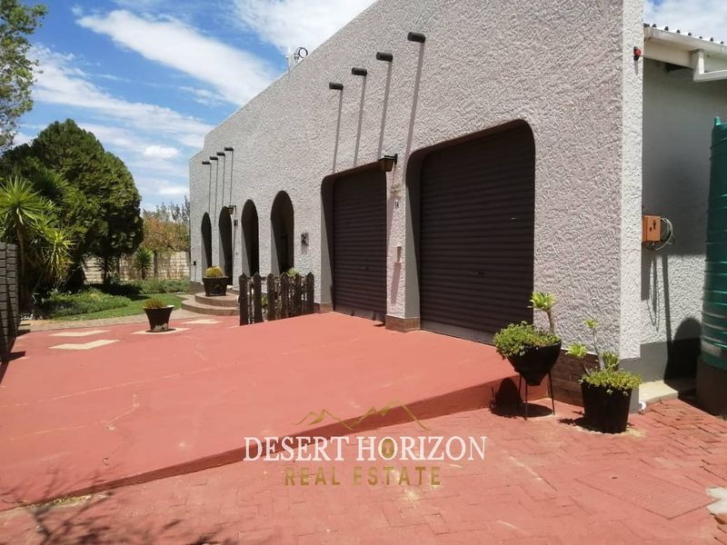 Front exterior view of the property featuring a double garage with roller shutter doors, textured facade, and a paved driveway area.