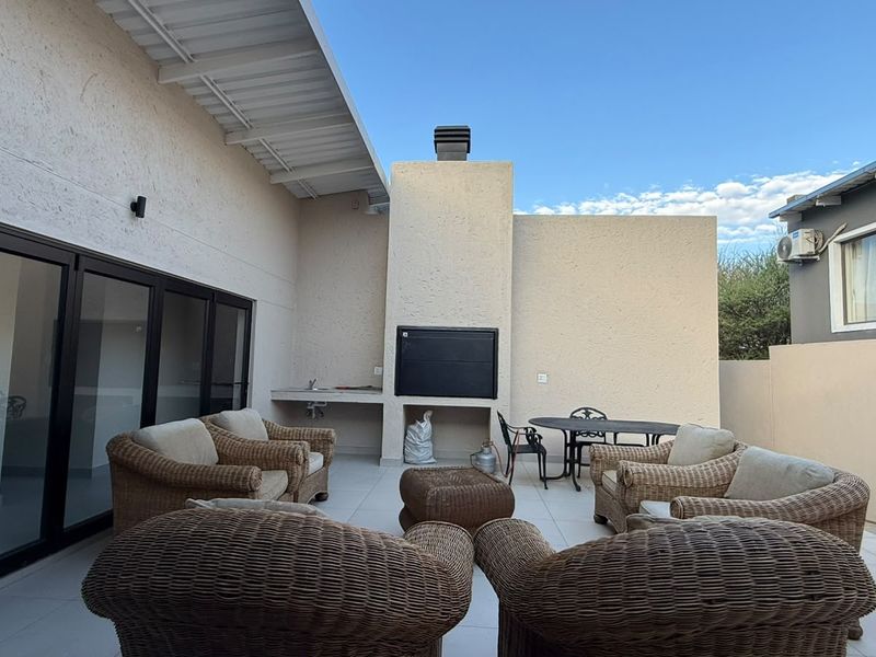 Spacious covered patio featuring a built-in braai, outdoor sink, and large sliding doors providing seamless access to the interior living space.