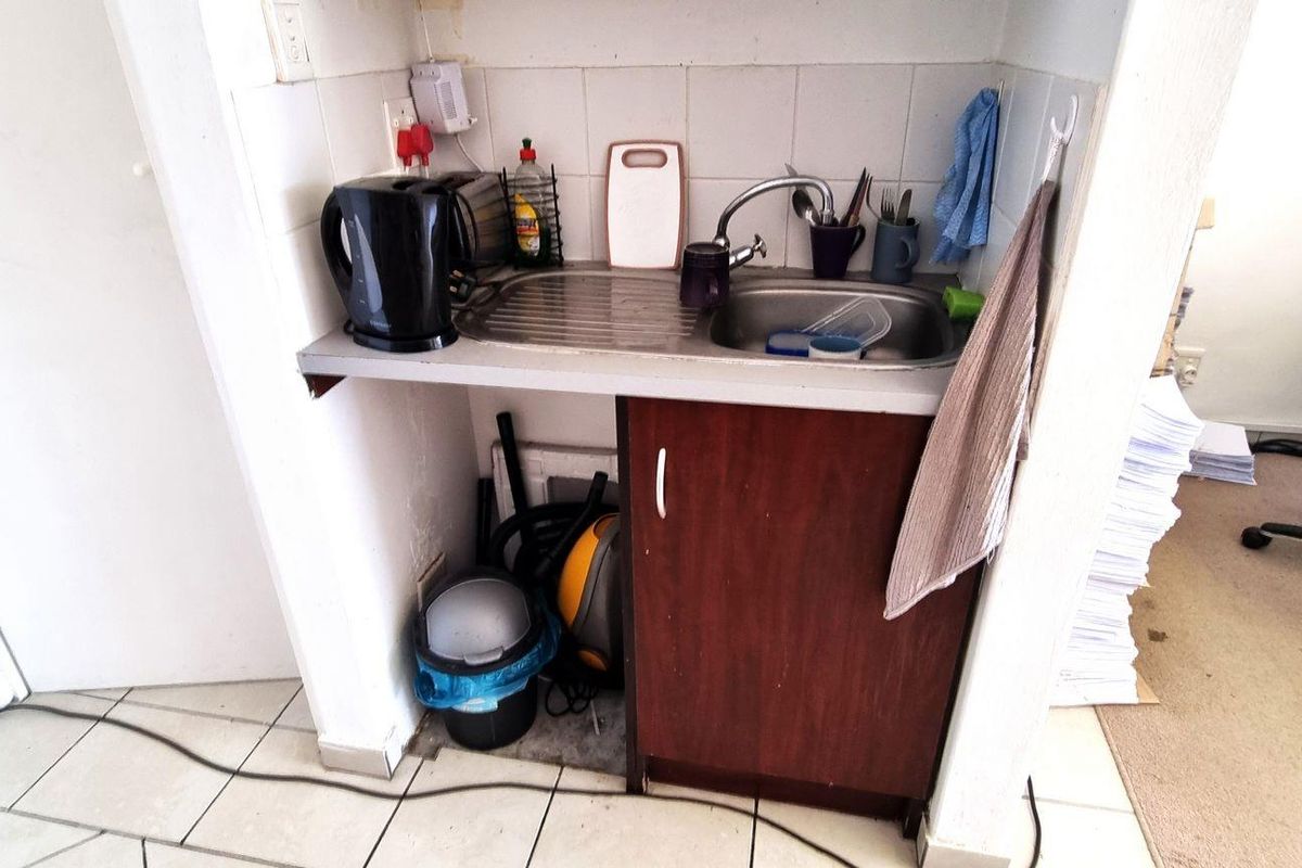 A compact kitchenette area featuring a single stainless steel sink, tiled backsplash, and a small base cabinet for storage.
