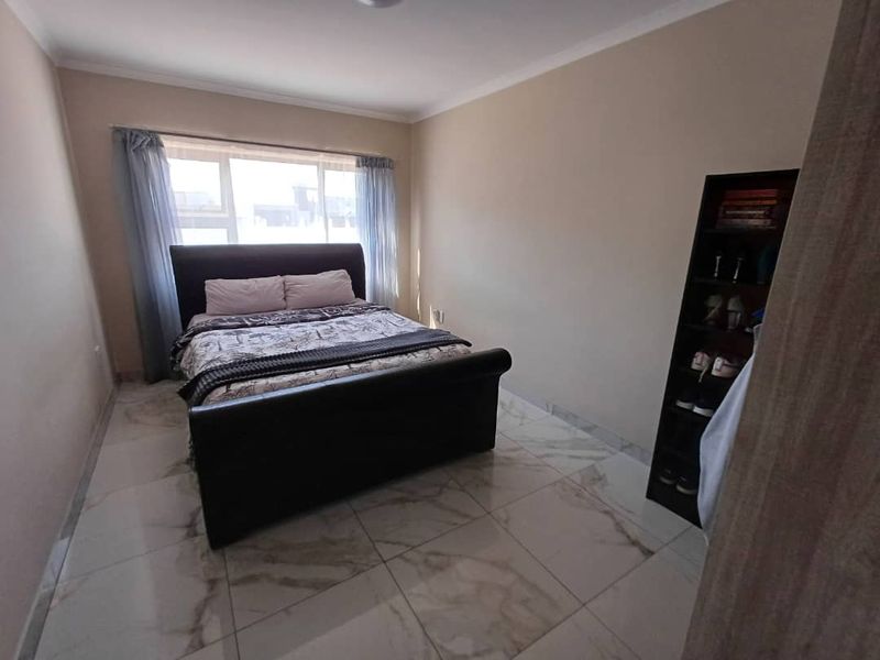 A bedroom featuring large format marble-look floor tiles, neutral wall paint, and a window with curtain tracks.