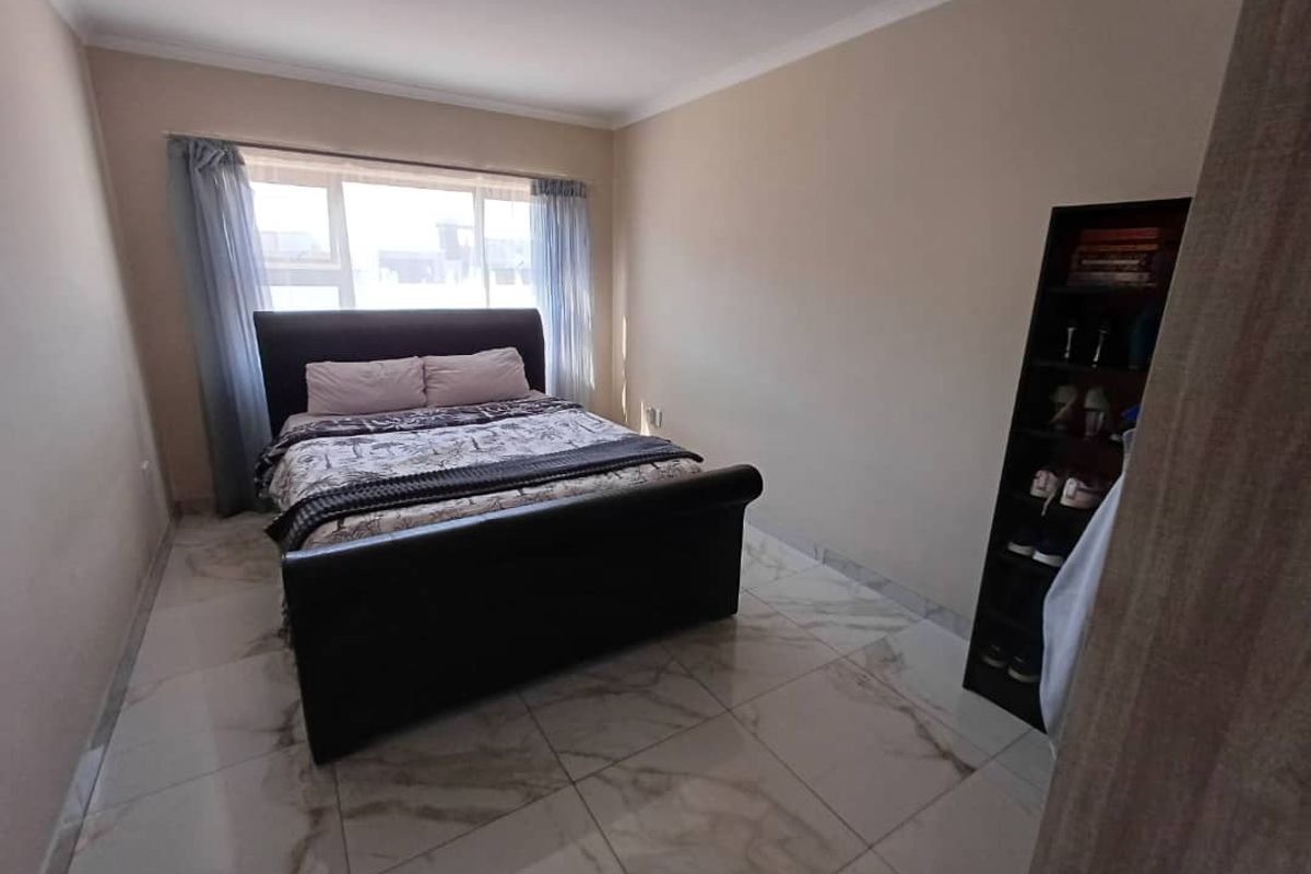 A bedroom featuring large format marble-look floor tiles, neutral wall paint, and a window with curtain tracks.