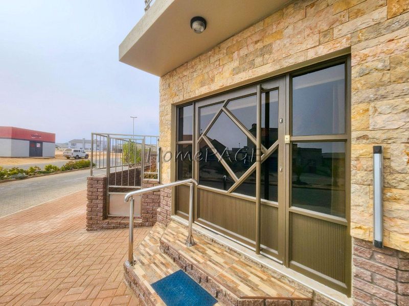 Front entrance featuring stone cladding, a modern sliding glass door with security frame, and a paved walkway with a stainless steel handrail.