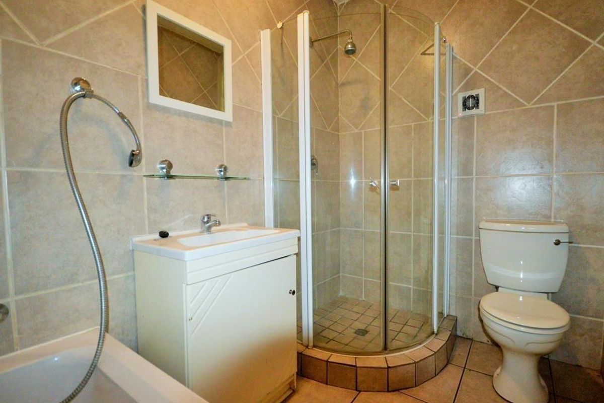 A functional bathroom featuring a corner shower enclosure, a separate bathtub, a vanity basin, and a toilet with neutral wall and floor tiling.