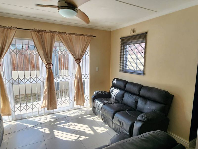 A living room featuring tiled flooring, a ceiling fan, and a sliding glass door with security gate leading to the exterior.