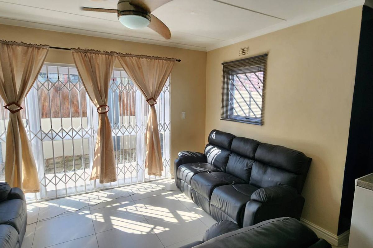 A living room featuring tiled flooring, a ceiling fan, and a sliding glass door with security gate leading to the exterior.