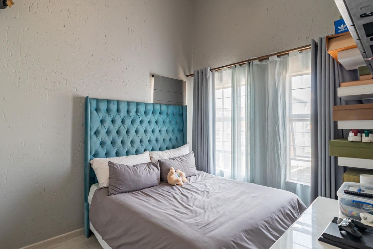 A bedroom featuring a tufted headboard, large windows with curtains, and neutral flooring.