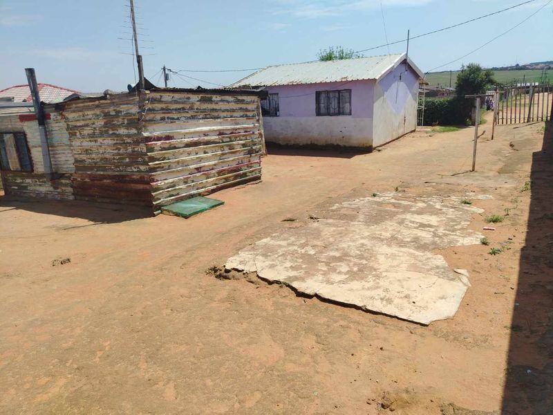 Rear yard area featuring a corrugated metal structure and a concrete slab foundation with surrounding dirt ground.