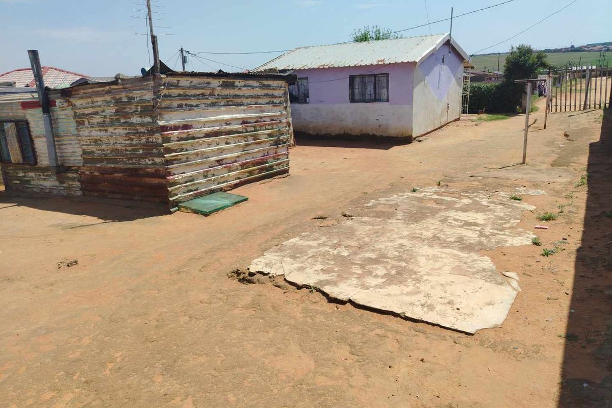 Rear yard area featuring a corrugated metal structure and a concrete slab foundation with surrounding dirt ground.