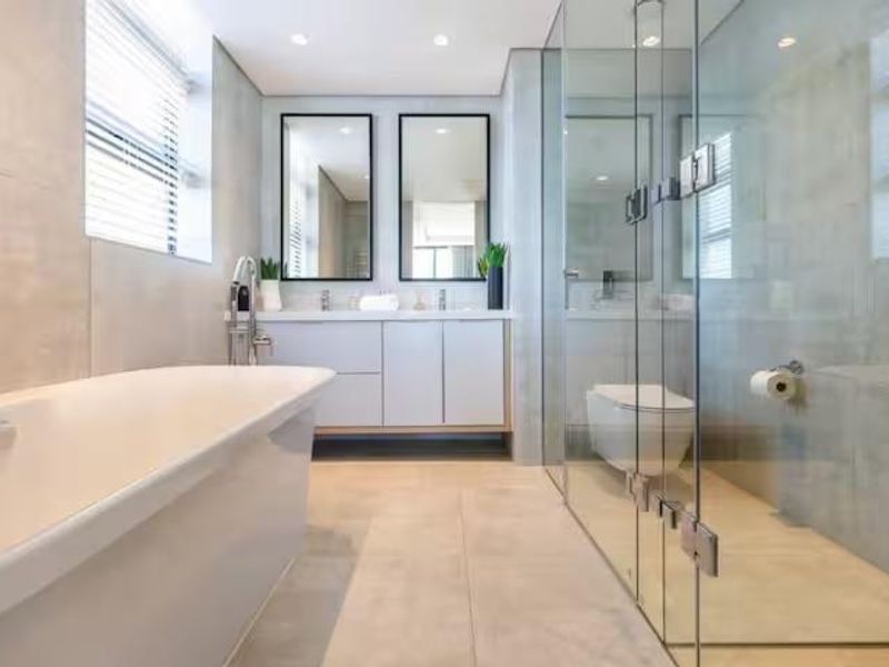 Modern bathroom featuring a sleek freestanding bathtub, double vanity with wall-mounted mirrors, and a spacious glass-enclosed shower with high-end finishes.