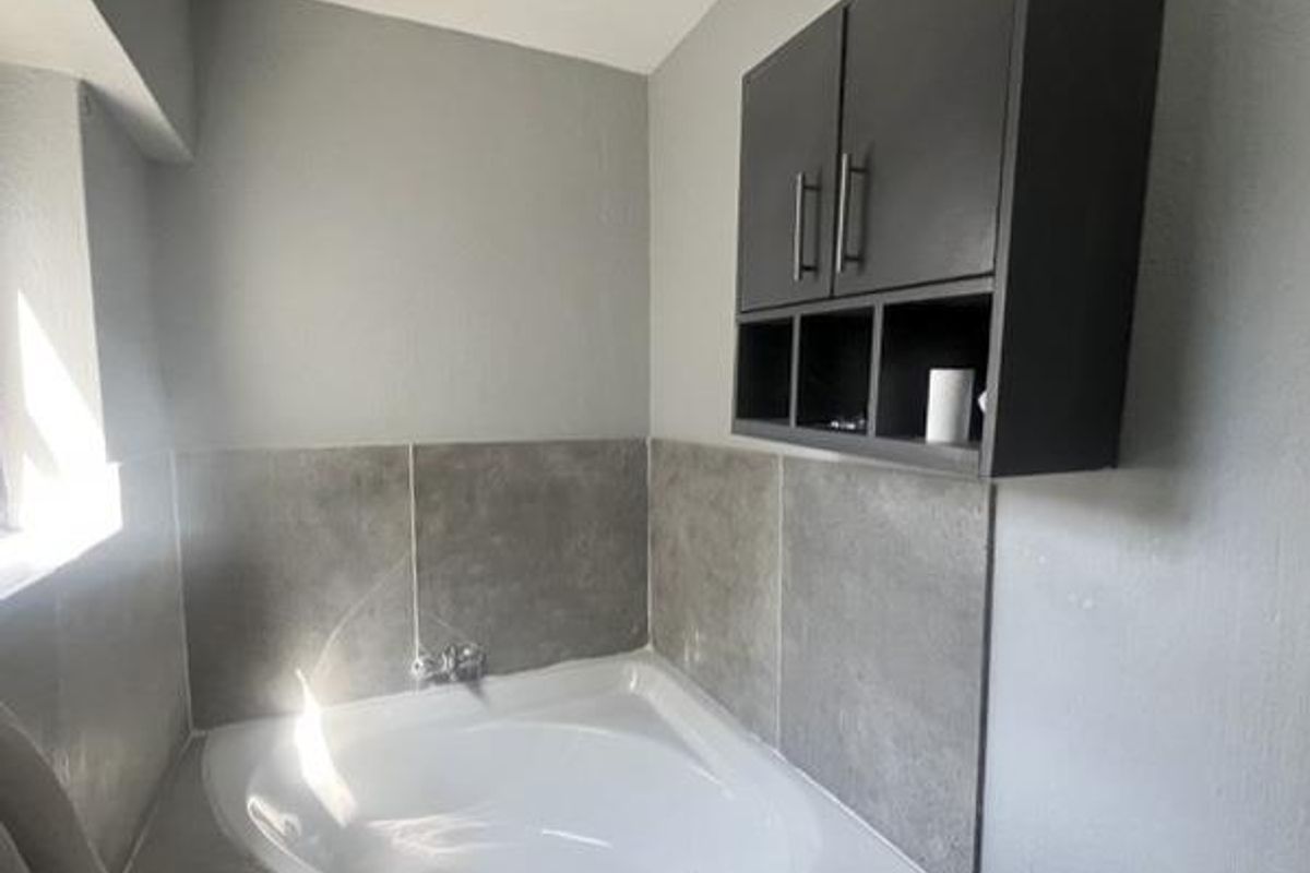 A bathroom featuring a corner bathtub with tiled splashback and a dark wall-mounted storage cabinet.