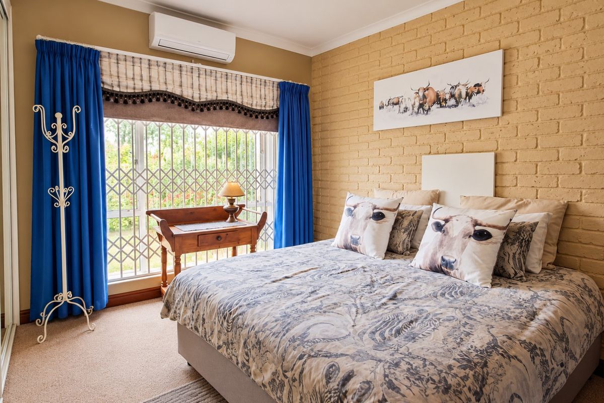 A bedroom featuring an exposed brick feature wall, carpeted flooring, and a wall-mounted split-system air conditioner for climate control.