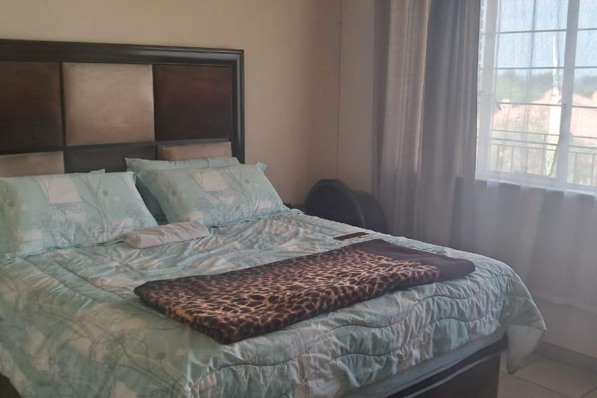 A bedroom featuring tiled flooring and a large window with security bars, providing natural light and a view of the surrounding complex.