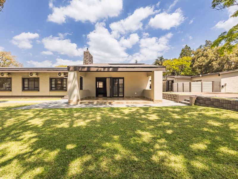 Rear view of the property featuring a covered patio, stone chimney, and a well-maintained lawn with paved pathways.