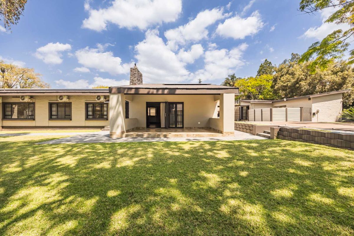 Rear view of the property featuring a covered patio, stone chimney, and a well-maintained lawn with paved pathways.