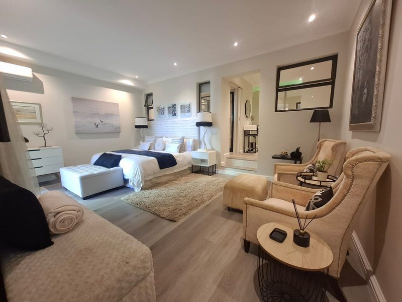 Spacious, well-appointed bedroom featuring modern laminate flooring, recessed downlighting, and an integrated air conditioning unit, with an adjoining ensuite area.