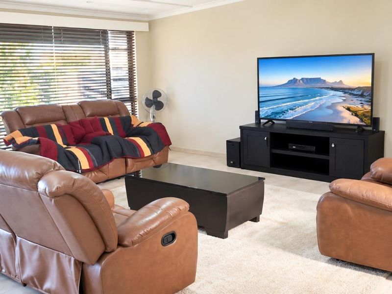 A well-lit living room featuring neutral tiled flooring, large windows with venetian blinds, and recessed ceiling lighting.