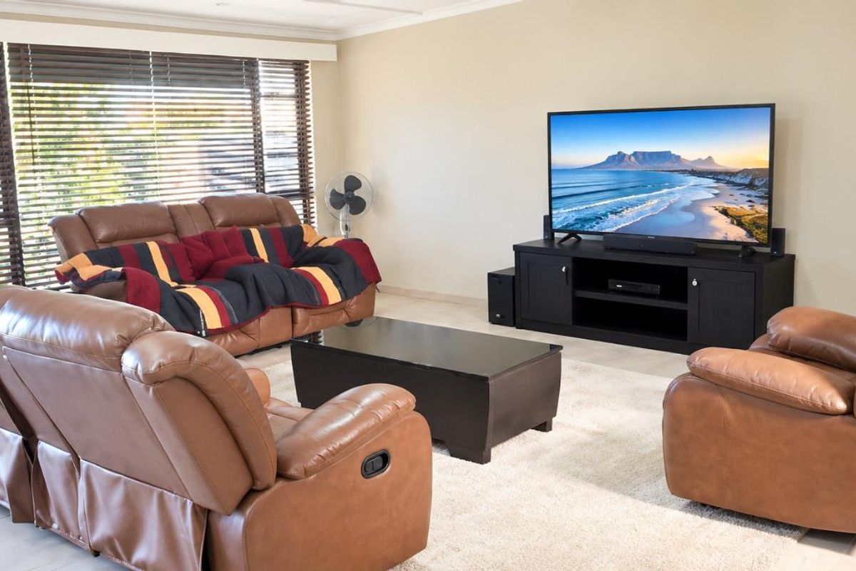 A well-lit living room featuring neutral tiled flooring, large windows with venetian blinds, and recessed ceiling lighting.