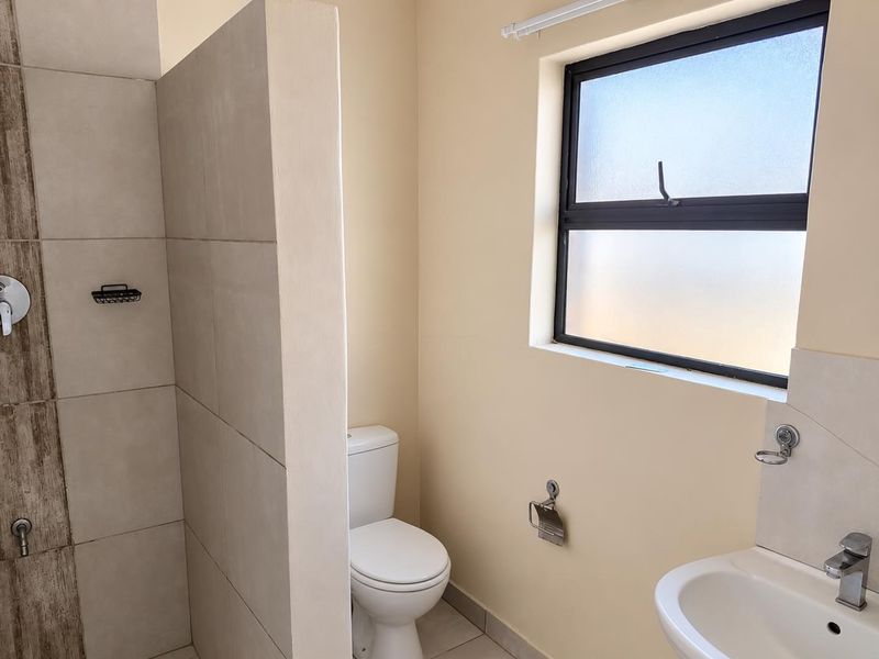 A clean, modern bathroom featuring a tiled shower enclosure, a white toilet, and a wall-mounted washbasin with a mixer tap.