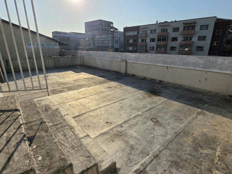 An open-air rooftop balcony featuring a concrete parapet wall with security spikes, offering an expansive outdoor space with urban views.
