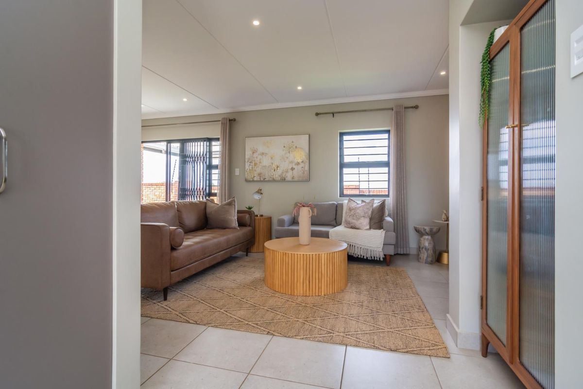 A bright and well-maintained living room featuring neutral tiled flooring, recessed downlighting, and large windows with security gates, offering a comfortable and inviting space.