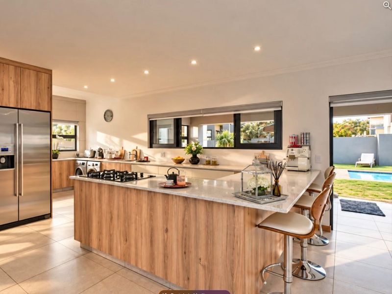 Modern open-plan kitchen featuring a large island with stone countertops, gas cooktop, wood-finish cabinetry, and direct access to the outdoor pool area.
