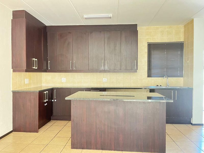 A functional kitchen featuring dark wood cabinetry, granite countertops, a central island, and tiled backsplash, offering a clean and practical workspace.