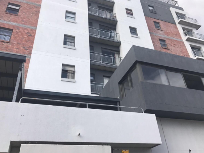 A low-angle view of a modern apartment building facade featuring a mix of brick and plastered finishes with multiple balconies.