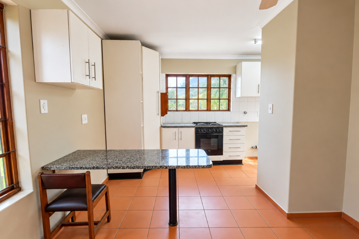 A functional kitchen featuring built-in cabinetry, granite countertops, a built-in oven and hob, and tiled flooring with a breakfast nook area.