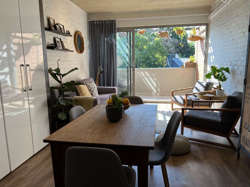 Open-plan living and dining area featuring exposed brick walls, concrete ceilings, and large sliding doors leading to a private balcony.