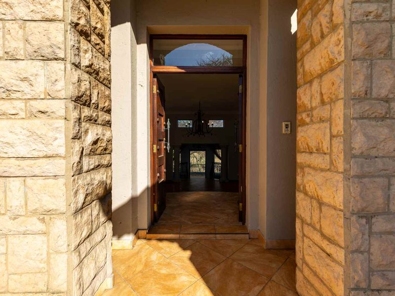 A welcoming entrance featuring natural stone cladding, tiled flooring, and a solid wood front door leading into the home.