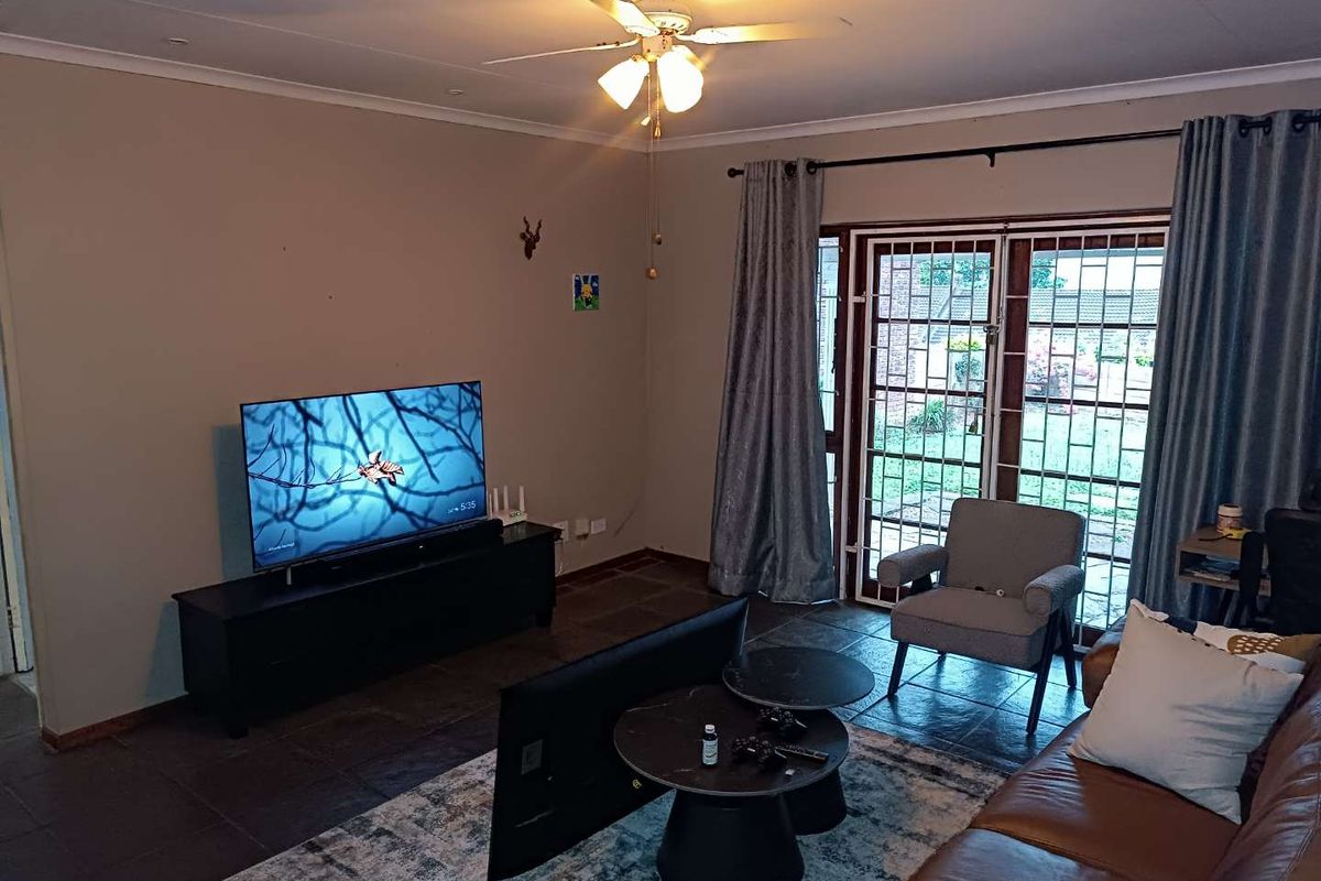 A living room featuring dark tiled flooring, a ceiling fan, and large glass sliding doors with security gates providing access to the exterior.