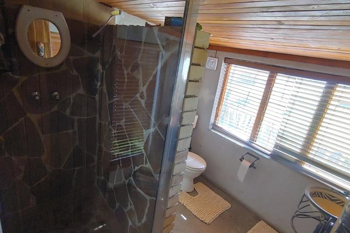A bathroom featuring a walk-in shower with stone tiling, a timber-clad ceiling, and a window with fitted blinds.