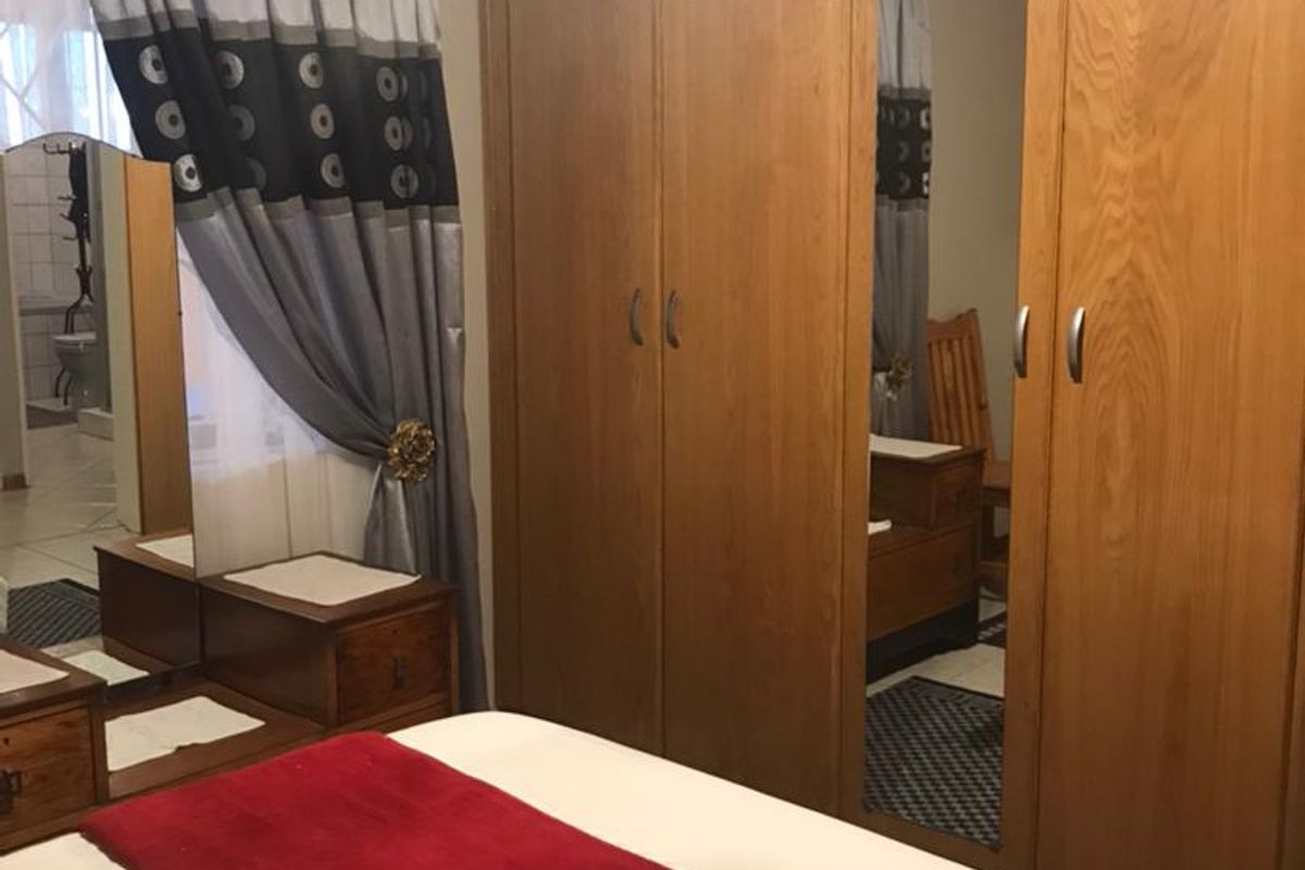 A bedroom featuring built-in wooden cupboards with a mirrored panel, providing ample storage space.