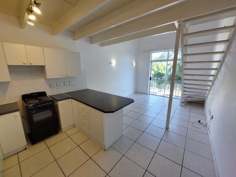 Open-plan kitchen and living area featuring tiled floors, exposed ceiling beams, a staircase, and direct access to a balcony through sliding glass doors.