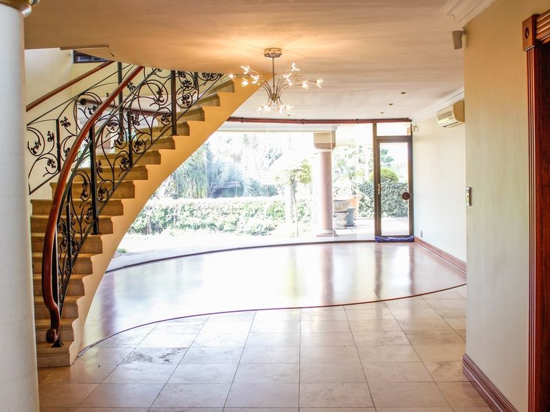 Spacious open-plan living area featuring a striking curved staircase with wrought iron detailing, tiled flooring, and direct access to the outdoor patio.