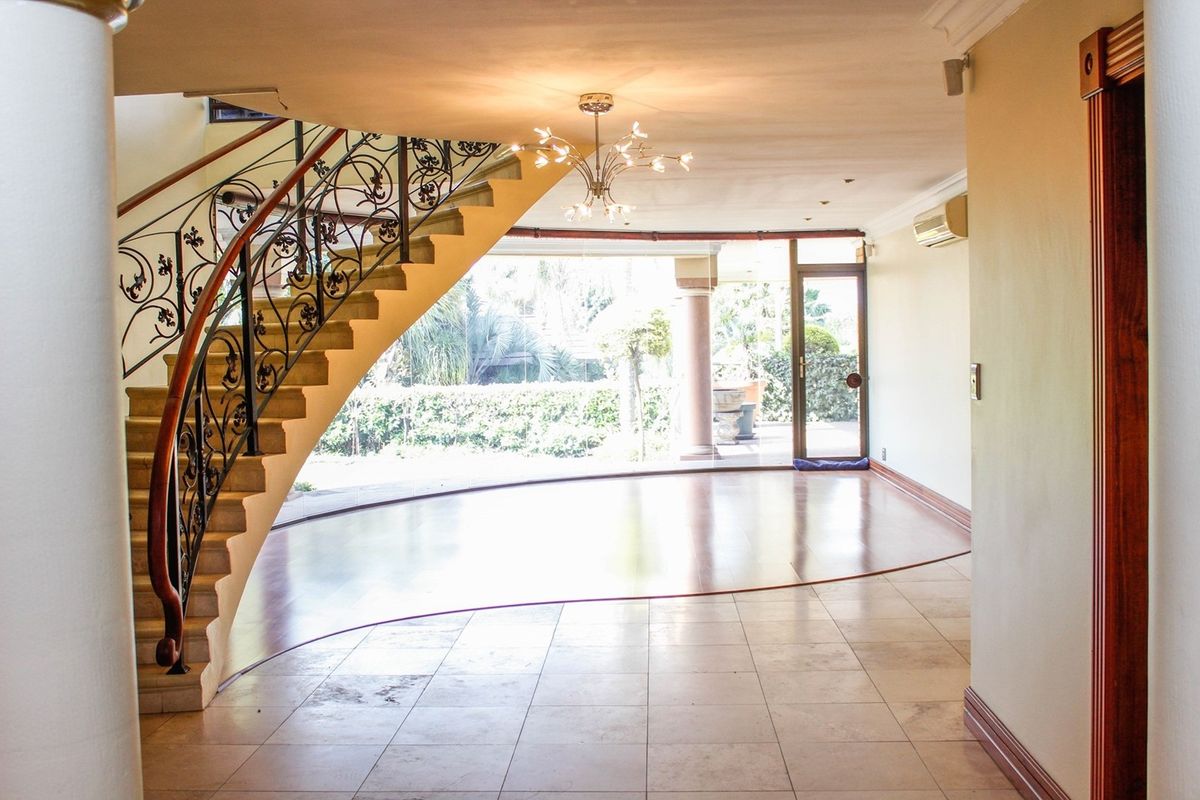Spacious open-plan living area featuring a striking curved staircase with wrought iron detailing, tiled flooring, and direct access to the outdoor patio.